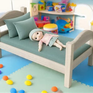 Könnte beinhalten: Ein kleines Holzbett mit einer matratze und Kissen in Salbeigrün. Eine Puppe in einem rosa Oberteil und blauem Rock liegt auf dem Bett. Der Raum hat einen blauen Boden und bunte Spielsachen.