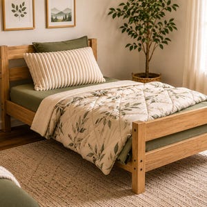 May include: A wooden bed frame with a green fitted sheet, a cream-colored, ribbed pillow, and a floral patterned comforter. The bed is in a well-lit room with a small side table and a potted plant.