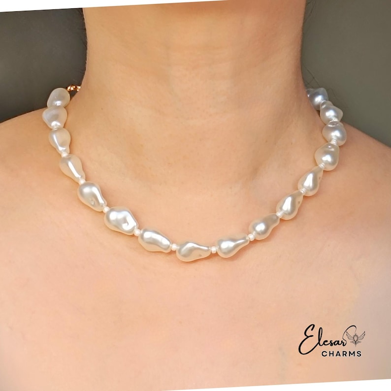 May include: A necklace featuring irregularly shaped, off-white pearls. The pearls are strung together, creating a choker-style design. The necklace is displayed on a person's neck, showcasing the jewelry's elegant and natural aesthetic. The brand name "Elesar Charms" is visible.