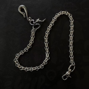 May include: A silver-toned chain with a hook clasp and a decorative snake charm. The chain is made of interlocking links and is displayed against a dark background. The hook clasp has a decorative design.