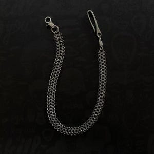 May include: A silver-colored wallet chain with a lobster clasp on one end and a hook on the other. The chain is made of small, interlocking rings. The background is a dark, textured surface.