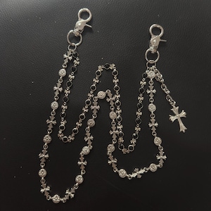 Puede incluir: Dos accesorios de cadena plateados con cierres de mosquetón. Cada cadena presenta una serie de pequeñas cruces, cuentas negras y detalles decorativos. Una cadena tiene un dije de cruz colgante.