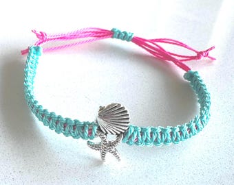 Puede incluir: Una pulsera de macramé turquesa con un cordón interior rosa y lazos ajustables. Un dije plateado con un diseño de concha y estrella de mar cuelga de la pulsera. Un accesorio de temática náutica.