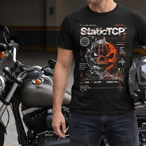 Può includere: Una t-shirt nera a maniche corte con una stampa grafica di una zucca stilizzata dal design meccanico e frastagliato. La stampa include testo tecnico e diagrammi, tra cui la parola StaticTCP, in inchiostro bianco e arancione sul petto.