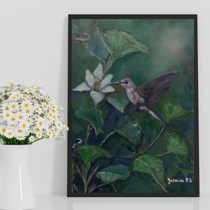 Può includere: Dipinto incorniciato di un colibrì vicino a un fiore bianco, circondato da foglie verdi. L'opera è firmata "Yasmine MK". Il dipinto è su una superficie bianca accanto a un vaso bianco pieno di margherite.