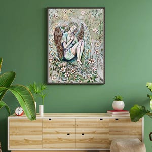 Può includere: Opera d'arte incorniciata raffigurante un angelo seduto con grandi ali, circondato da fiori e fogliame. L'angelo indossa un abito azzurro. L'opera è ambientata su uno sfondo verde.