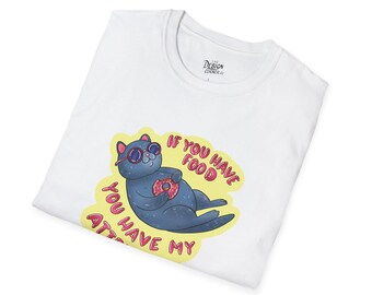 Op de afbeelding: Wit T-shirt met een cartoon otter ontwerp. De blauwe otter draagt een zonnebril en houdt een donut vast. Tekst op het shirt luidt: "Als je eten hebt, heb je mijn aandacht."