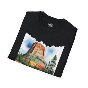 Könnte beinhalten: Schwarzes T-Shirt mit einer Aquarellillustration einer großen Felsformation, wahrscheinlich ein Berg oder eine Butte, und einem Wald. Das Bild hat einen weißen Rand. Der Text "THE DESIGN CORNER CO." ist auf dem T-Shirt aufgedruckt.