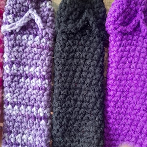 Puede incluir: Primer plano de varias zapatillas de ganchillo hechas a mano en varios colores. Las zapatillas son en tonos morados y negros. La puntada de ganchillo es visible y las zapatillas parecen suaves y cómodas.