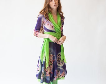 May include: A woman wearing a purple and green wrap dress with a floral print. The dress has a green sash tied at the waist. She is wearing green tights and has long red hair.