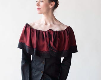 May include: A black off-the-shoulder top with a red ruffled collar and long sleeves. The top is paired with a black skirt.