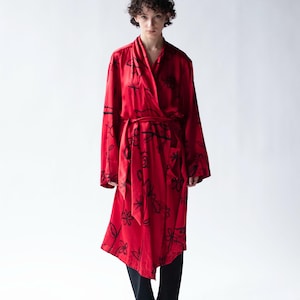 Puede incluir: Una bata roja con un estampado floral negro. La bata tiene mangas largas y un dise&ntilde;o envolvente con un cintur&oacute;n a juego. El modelo lleva pantalones y zapatos negros.