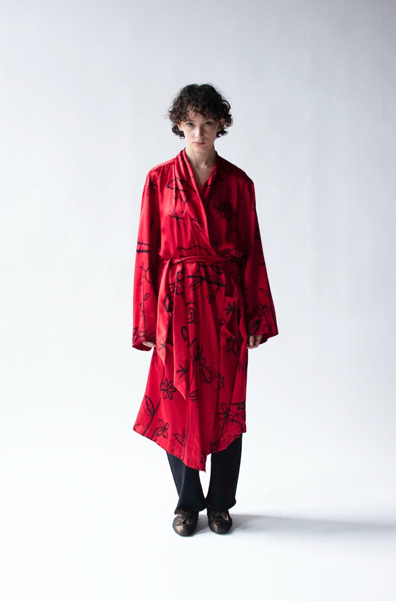 Puede incluir: Una bata roja con un estampado floral negro. La bata tiene mangas largas y un dise&ntilde;o envolvente con un cintur&oacute;n a juego. El modelo lleva pantalones y zapatos negros.