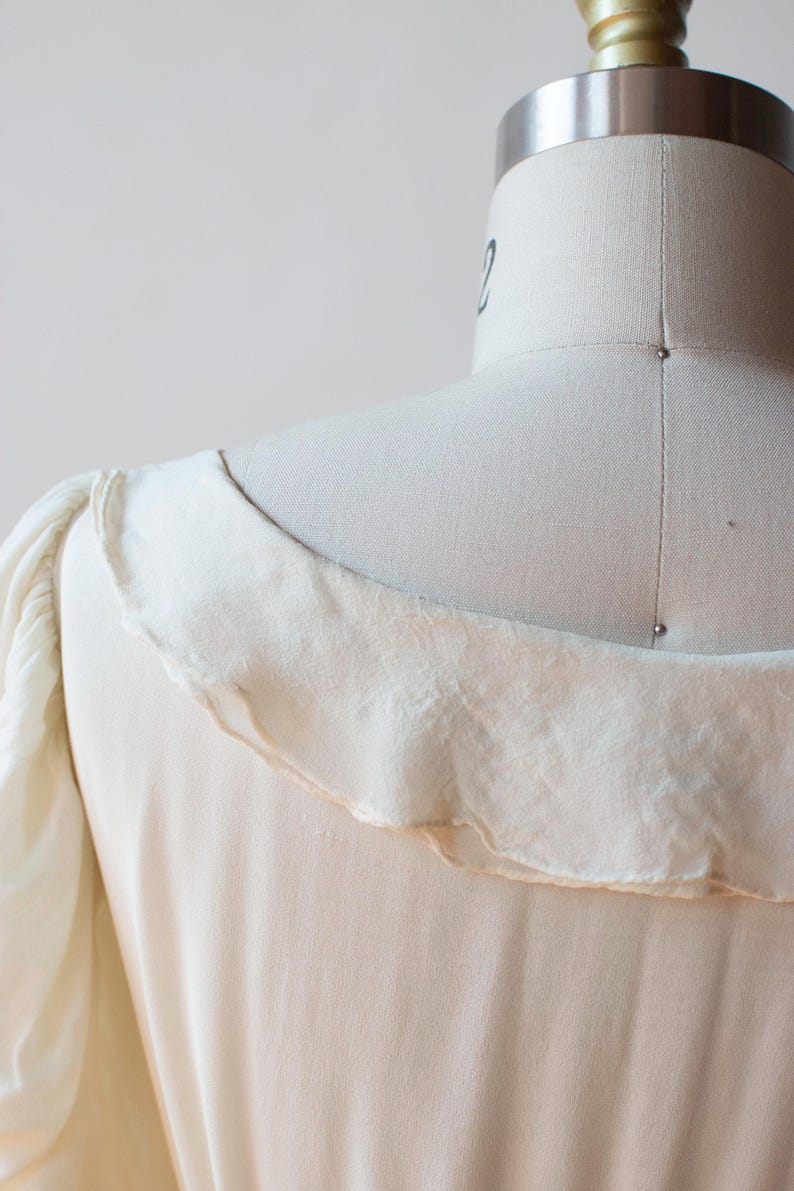 May include: A white vintage dress with a ruffled neckline and puffed sleeves.