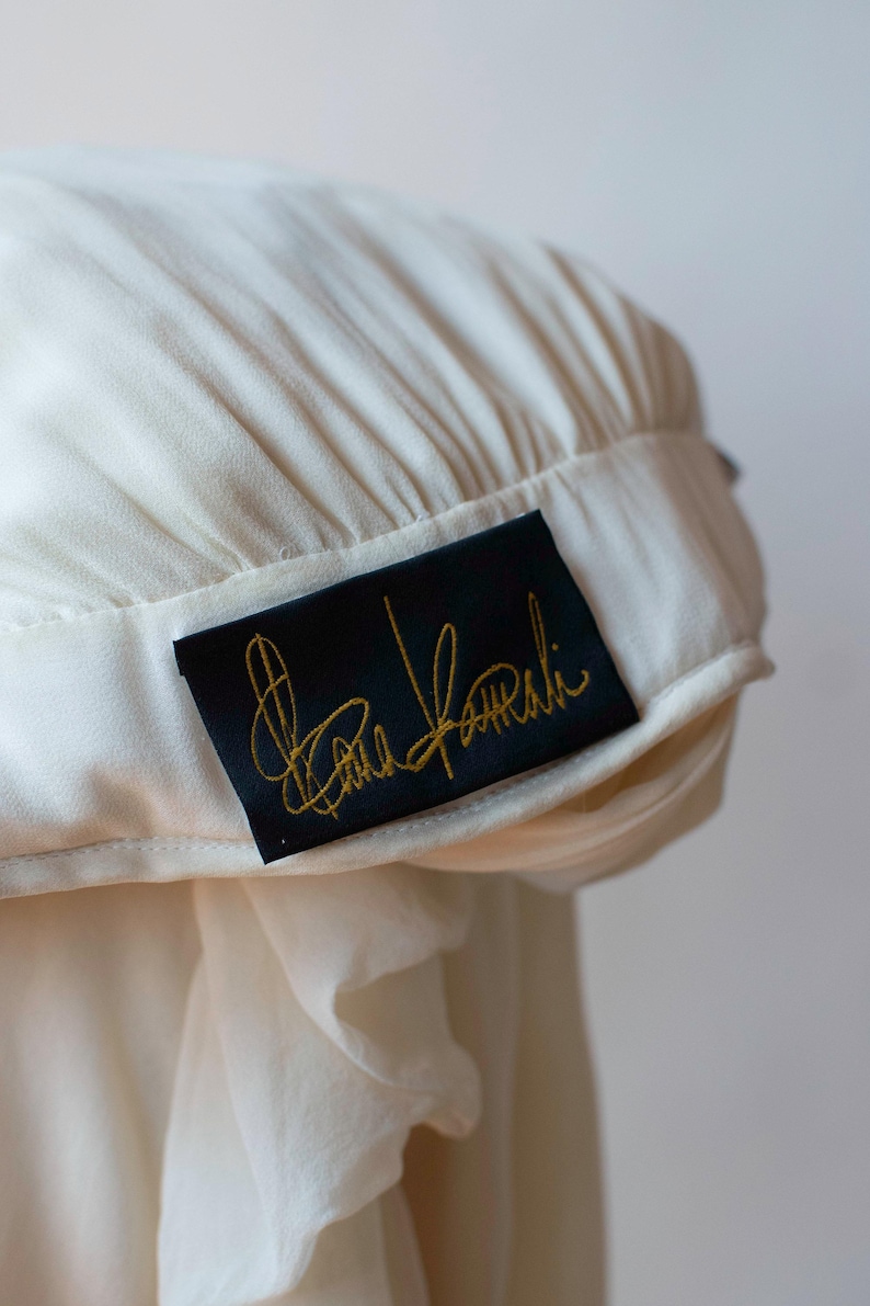 May include: A white garment with a black label that says "Carla Falini" in gold lettering.