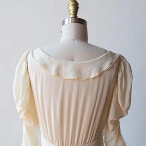May include: A white, long-sleeved dress with a ruffled collar and cuffs. The dress has a fitted bodice and a flowing skirt.