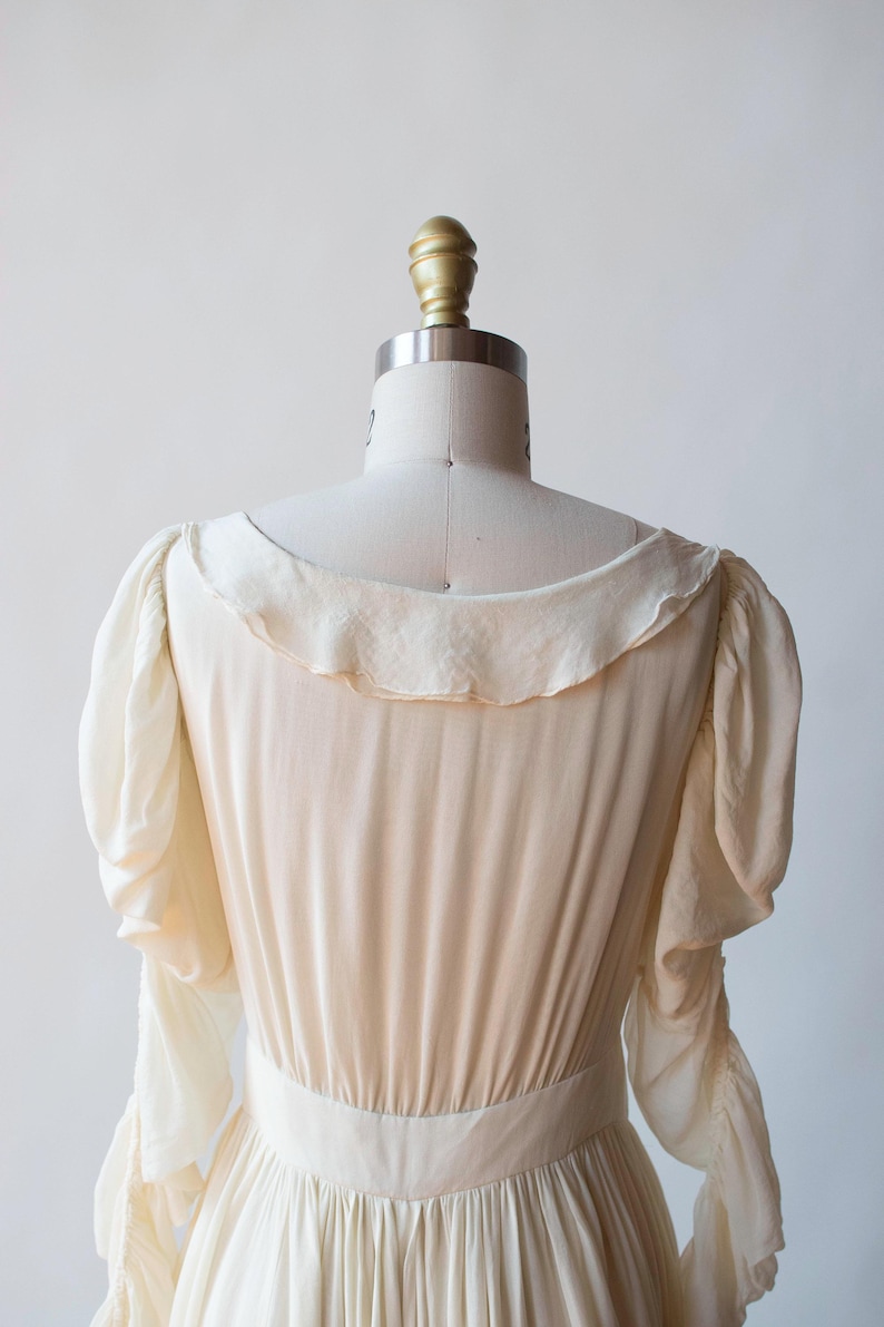 May include: A white, long-sleeved dress with a ruffled collar and cuffs. The dress has a fitted bodice and a flowing skirt.