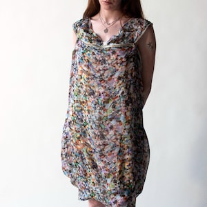 Pode incluir: Vestido sem mangas com padrão floral colorido. Apresenta decote redondo com fecho de correr dourado e saia balão. O tecido, transparente e leve, exibe uma mistura de cores como azul, rosa e amarelo.