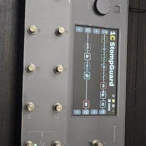 May include: A gray 1C StompGuard pedal with multiple silver knobs and buttons. The device has a screen displaying various icons and settings. The text "QUADCORTEX" is visible on the bottom right.