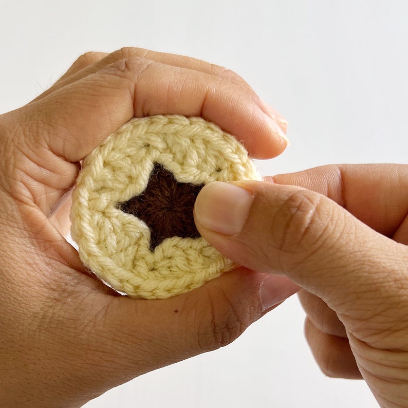 May include: A crocheted star-shaped coaster with a brown center. The coaster is being held in a person's hand.