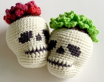 Peut inclure: Deux décorations en forme de crâne crochetées. Les crânes sont blanc cassé avec des orbites et des dents gris foncé. Un crâne a des cheveux crochetés rouges et roses, l'autre a des cheveux crochetés verts. Les crânes sont faits à la main.