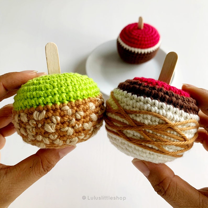 Puede incluir: Dos juguetes de crochet con forma de manzana con palos de madera. Una manzana es verde y marr&oacute;n, la otra es marr&oacute;n, blanca y roja.