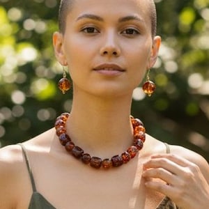 May include: A woman wearing a necklace and earrings made of amber-colored beads. The necklace is a choker style, and the earrings are dangling. The woman is wearing a green spaghetti strap dress.