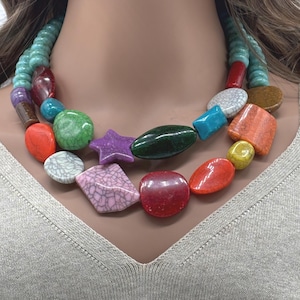 May include: A colorful statement necklace featuring large, irregularly shaped beads in various colors, including red, green, purple, and turquoise. The necklace has a layered design with a turquoise beaded strand at the top.