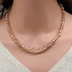May include: A delicate necklace featuring faceted, light brown beads strung on a gold-colored chain. The beads vary in size, creating a subtle, elegant design. The necklace is displayed on a mannequin, showcasing its length and style. A simple, yet sophisticated jewelry piece.