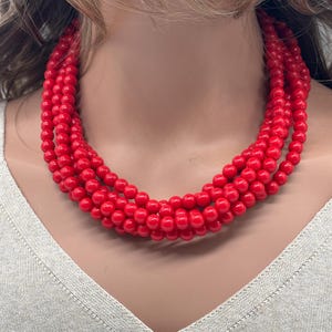 May include: A multi-strand necklace featuring vibrant red beads. The necklace is composed of several strands of round, glossy beads, creating a bold and eye-catching accessory. The beads are a solid, bright red color, offering a pop of color.