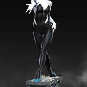 May include: A statue of a female superhero in a black and white bodysuit with a spider-web design. She has blonde hair and is standing on a rooftop base. Her boots are a bright blue colour.