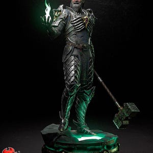 Puede incluir: Una detallada figura de un guerrero con una armadura ornamentada, sosteniendo una llama verde brillante. La figura tiene una larga barba blanca y ojos verdes. La base también está iluminada con luz verde, y un gran martillo descansa cerca.