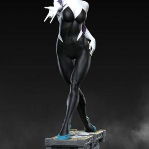 May include: A statue of a female superhero in a black and white bodysuit with a spider-web design. The figure has blonde hair and is wearing white gloves and blue shoes. The statue is standing on a detailed, brick-like base.
