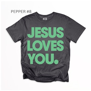 K&ouml;nnte beinhalten: Ein dunkelgraues T-Shirt mit dem Text "JESUS LOVES YOU" in gro&szlig;en, leuchtend gr&uuml;nen Buchstaben. Das Shirt hat auch den Text "PEPPER #8" in der oberen linken Ecke. Das Shirt ist ein Rundhals und hat kurze &Auml;rmel.