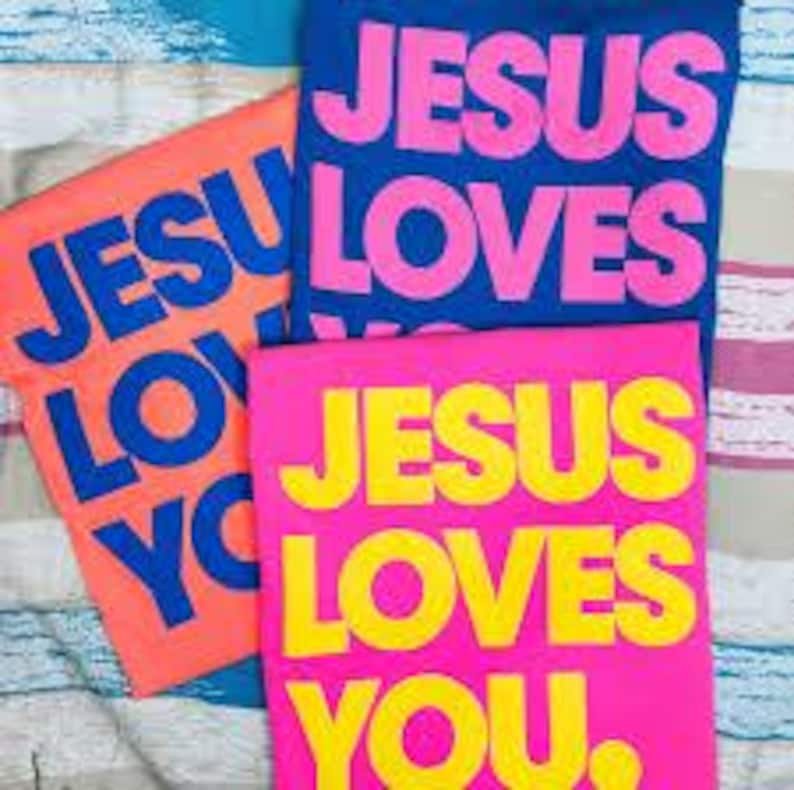 K&ouml;nnte beinhalten: Drei T-Shirts mit der Aufschrift "JESUS LOVES YOU" in fetten Buchstaben. Ein Shirt ist orange mit blauem Text, ein anderes ist blau mit pinkfarbenem Text und das dritte ist pink mit gelbem Text. Die Shirts sind auf einer gestreiften Oberfl&auml;che gefaltet.