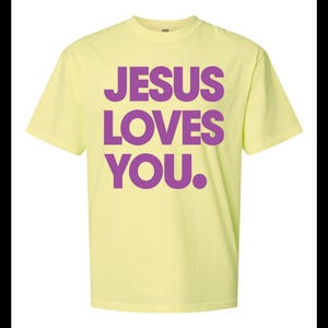 K&ouml;nnte beinhalten: Hellgelbes T-Shirt mit dem Text "JESUS LOVES YOU." in gro&szlig;en, lila Buchstaben. Das kurz&auml;rmelige T-Shirt hat einen Rundhalsausschnitt. Der Text ist mittig auf der Vorderseite des Kleidungsst&uuml;cks platziert.