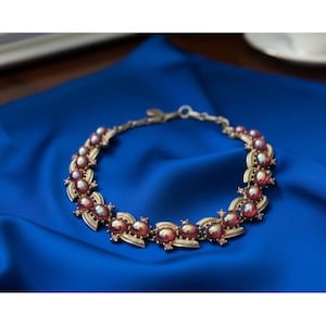 May include: A gold-toned bracelet with oval, iridescent pink gemstones. The bracelet is set against a vibrant blue fabric, highlighting the intricate design and color of the jewelry. The clasp is visible, indicating a secure closure.