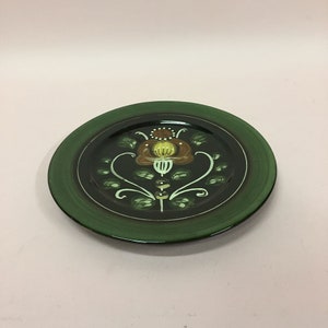 May include: A green ceramic plate with a brown and yellow floral design. The plate has a dark green rim and a black center.