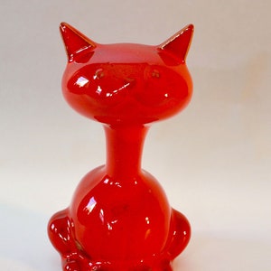 Può includere: Una statuetta di gatto in ceramica rosso vivo con una finitura lucida. Il gatto ha un collo lungo e un corpo arrotondato.