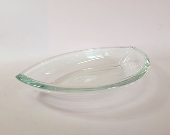 May include: A clear glass serving dish shaped like a boat. The dish is oval and has a slight curve to it.