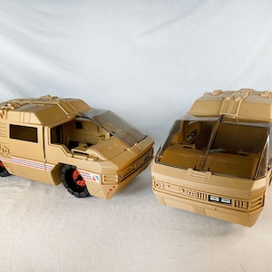Puede incluir: Dos vehículos de juguete vintage en color arena con ventanas de plástico transparente. El vehículo de la izquierda tiene el texto "GCH" en el lateral. Ambos vehículos tienen un diseño futurista.