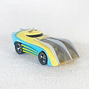 May include: A yellow and blue toy car with a clear plastic top and the word "REBEL" printed on the top. The car has black wheels and a black stripe on the side.