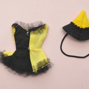 May include: A black and yellow doll dress with a black tulle skirt and a matching yellow hat with a black brim.