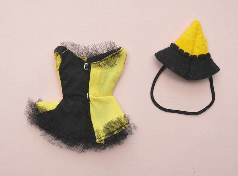 May include: A black and yellow doll dress with a black tulle skirt and a matching yellow hat with a black brim.
