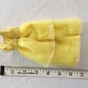 May include: A yellow sheer dress with white lace trim. The dress is about 6 inches long.