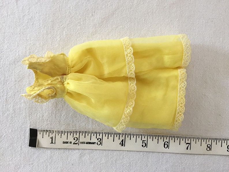 May include: A yellow sheer dress with white lace trim. The dress is about 6 inches long.