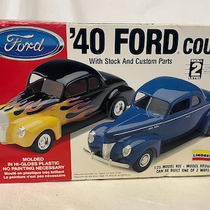May include: A model kit box featuring two '40 Ford Coupe cars. One car is black with yellow flames, the other is blue. The box has the Ford logo and text that reads "'40 Ford Coupe" and "1/25 Model Kit".