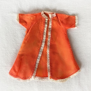 May include: A bright orange doll's dress with white lace trim around the neckline, sleeves, and hem.