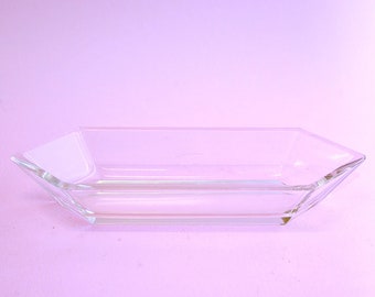 May include: A clear glass rectangular dish with a geometric shape. The dish has a slightly raised edge and is made of clear glass.