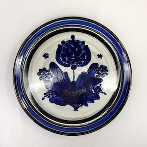 May include: A white ceramic plate with a blue and black floral design. The plate has a black rim with a blue stripe.